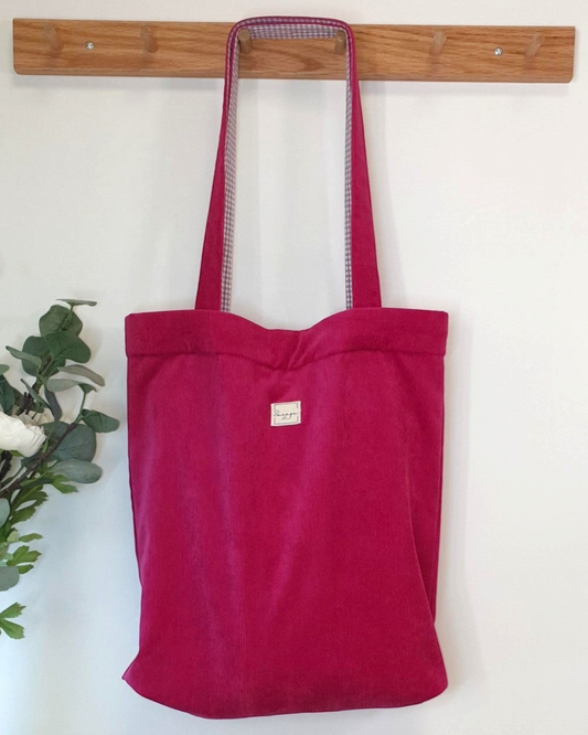 Tote bag SAVAGE LINE de pana fina fucsia con interior de cuadros vichy y cierre magnético colgado en un perchero