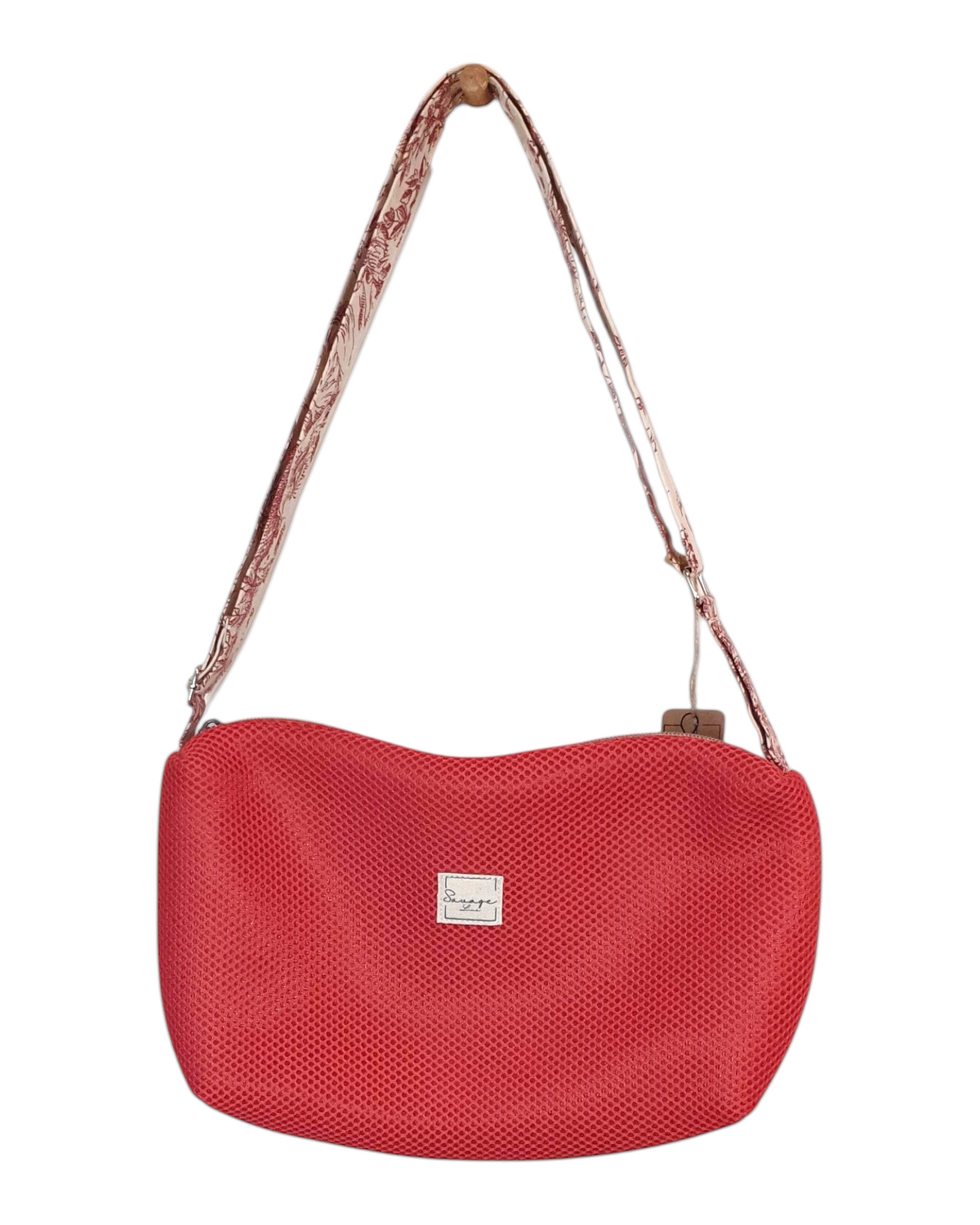 Bandolera SAVAGE LINE Sara Cross roja de mesh 3D con correa de loneta estampada colgada en un perchero de madera